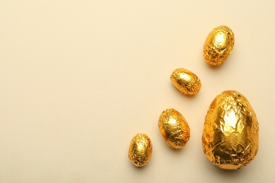 Chocolate eggs wrapped in golden foil on beige background, flat lay. Space for text