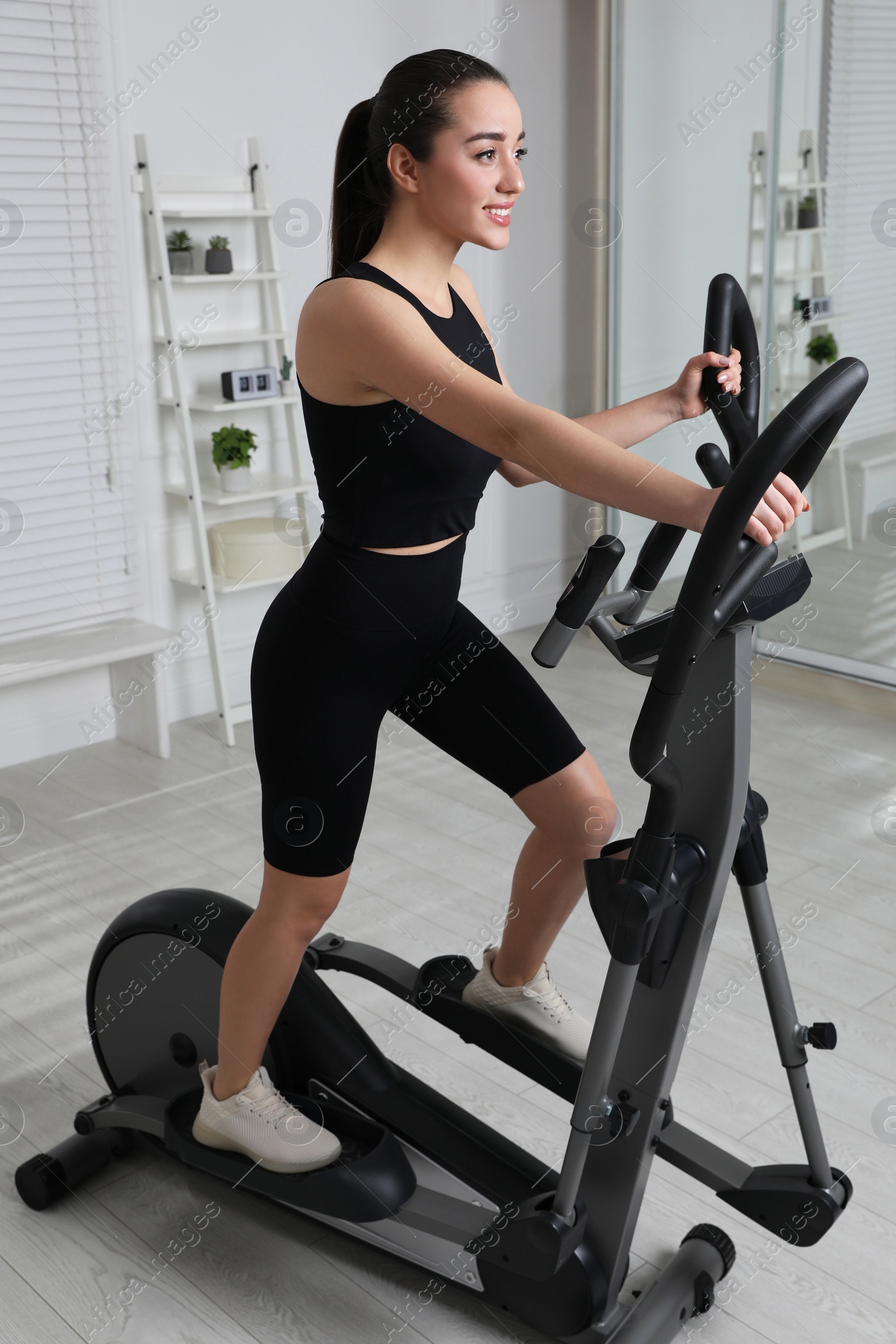 Photo of Happy young woman training on elliptical machine at home