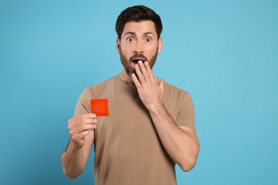 Photo of Emotional man holding condom on light blue background. Safe sex