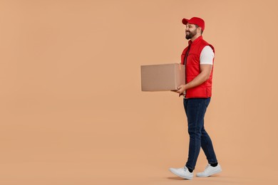 Photo of Happy young courier with parcel on light brown background, space for text