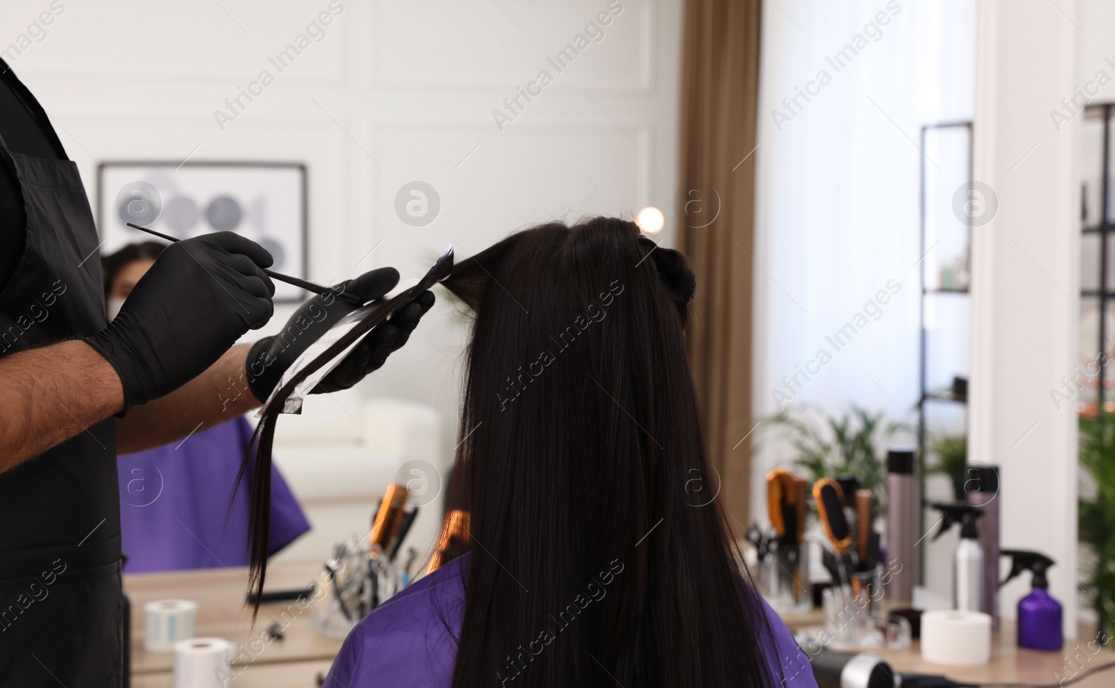 Photo of Professional stylist working with client in salon, back view. Hairdressing services during Coronavirus quarantine