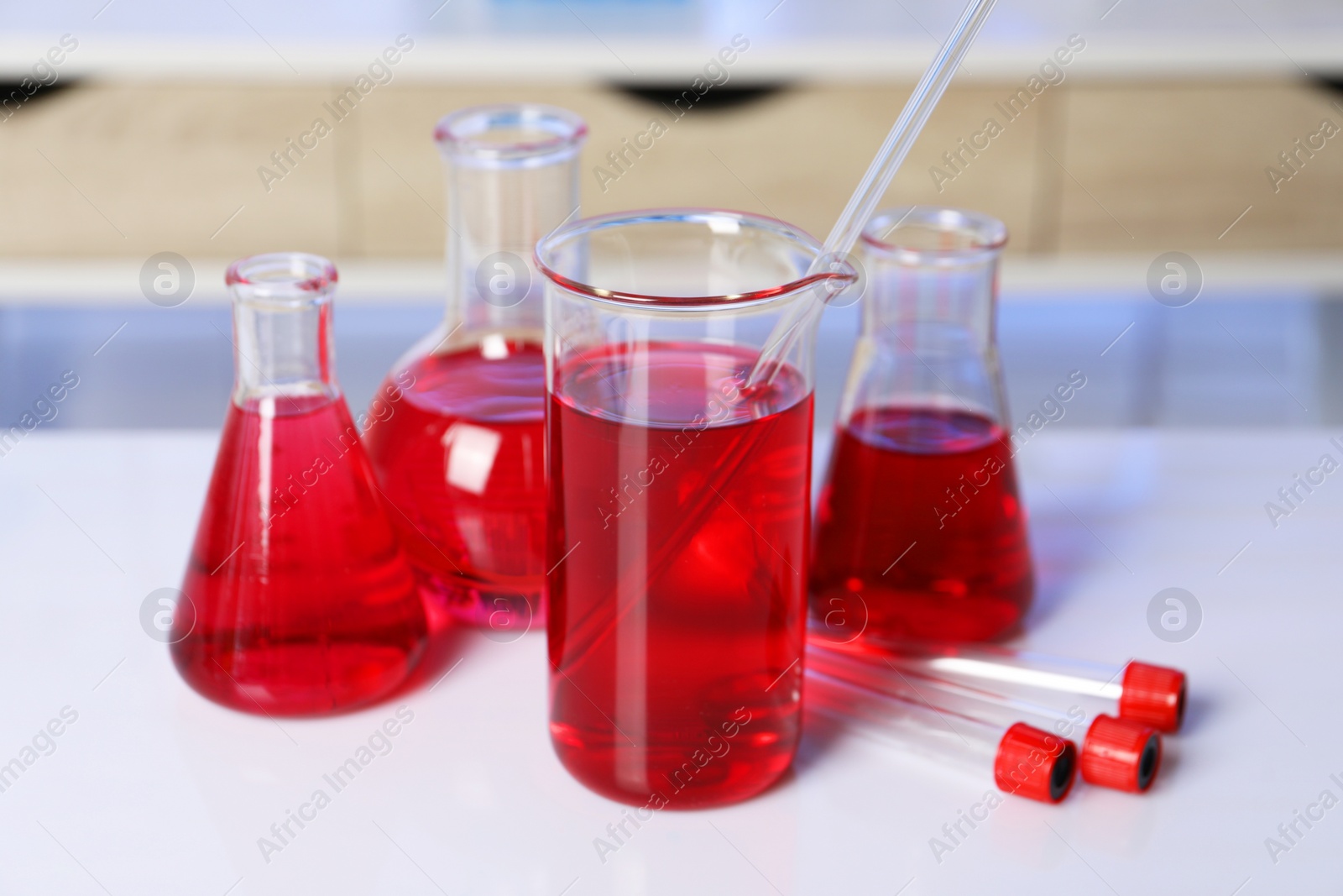 Photo of Laboratory analysis. Different glassware with red liquid on white table indoors