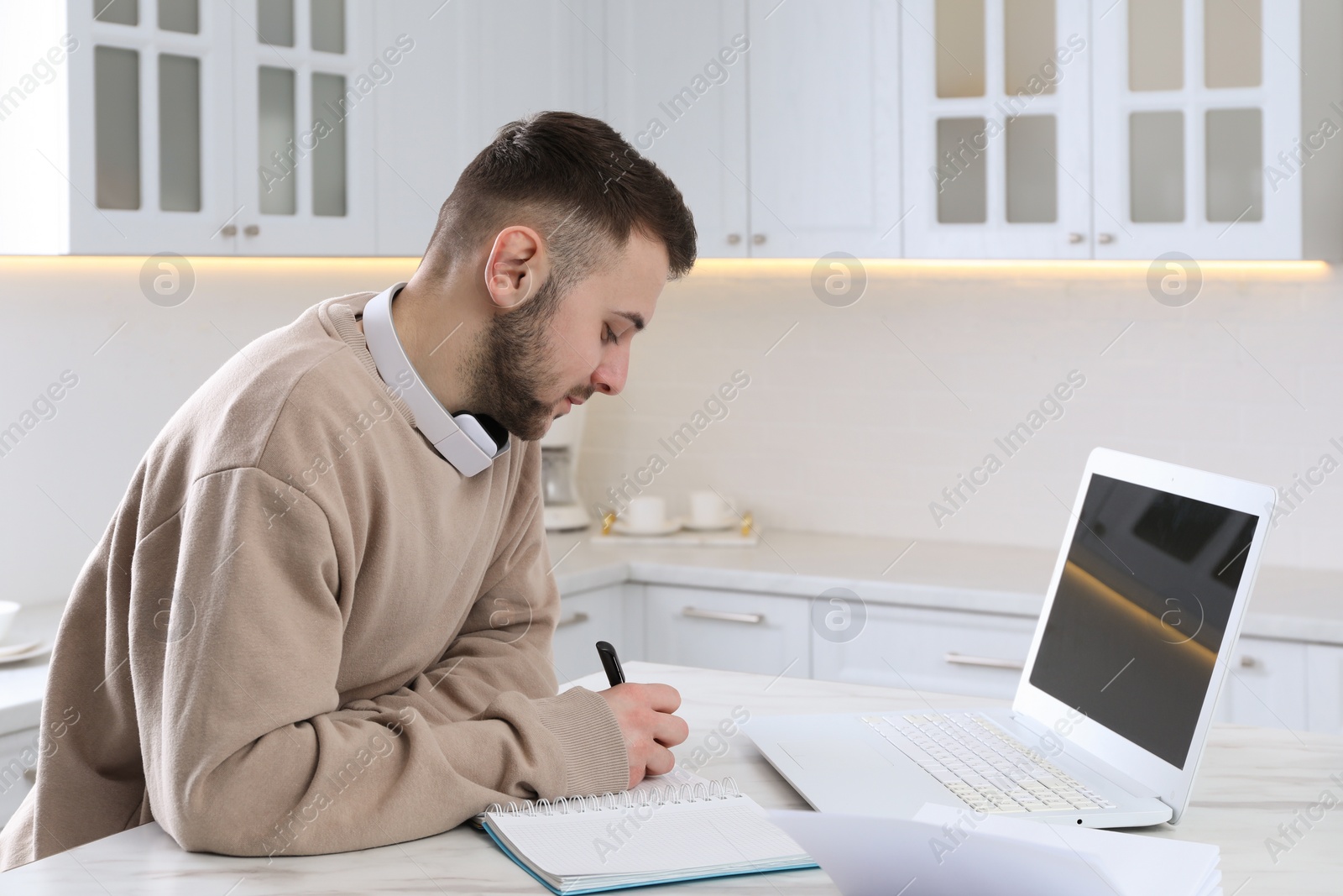 Photo of Young man using modern laptop for studying in kitchen. Distance learning