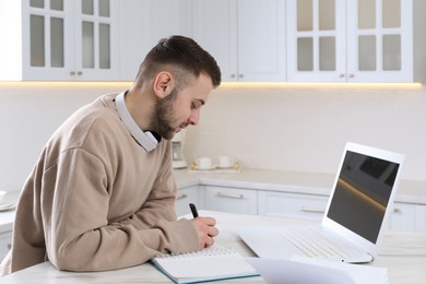 Young man using modern laptop for studying in kitchen. Distance learning