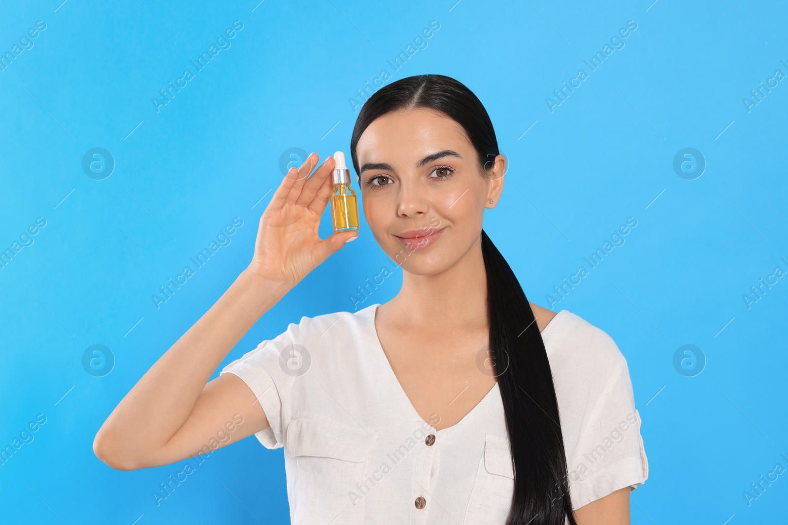 Photo of Young woman with bottle of essential oil on light blue background