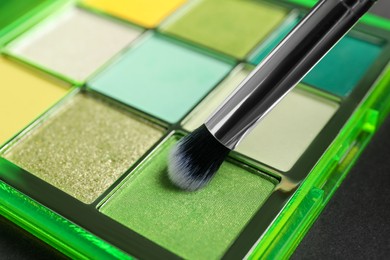 Photo of Colorful eyeshadow palette with brush on dark background, closeup