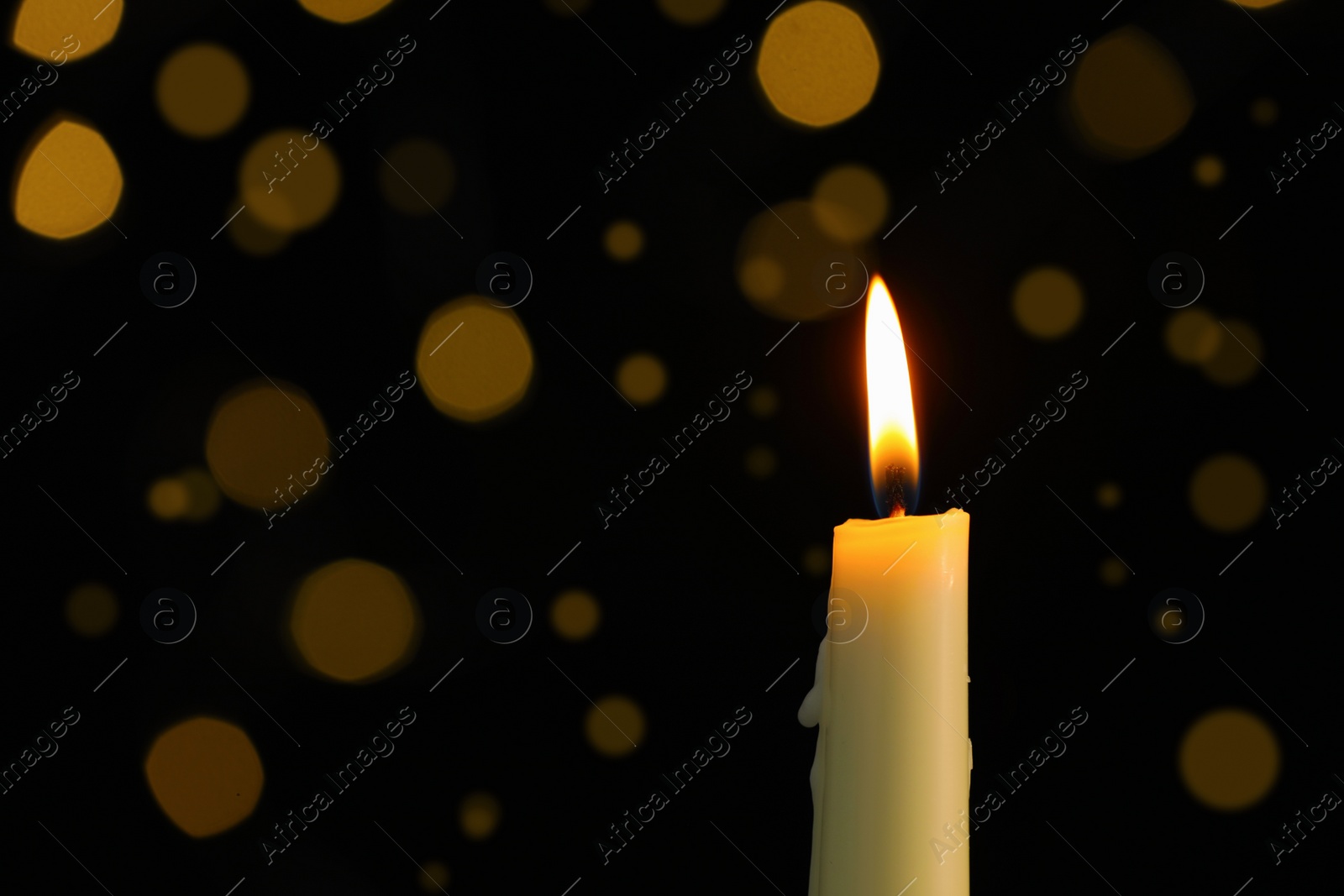 Photo of Wax candle burning against blurred lights in darkness, closeup. Space for text