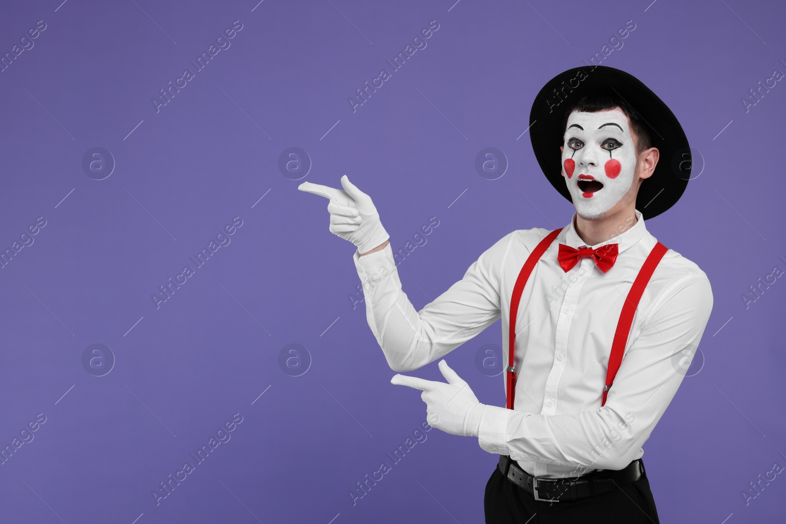 Photo of Funny mime artist pointing at something on purple background. Space for text