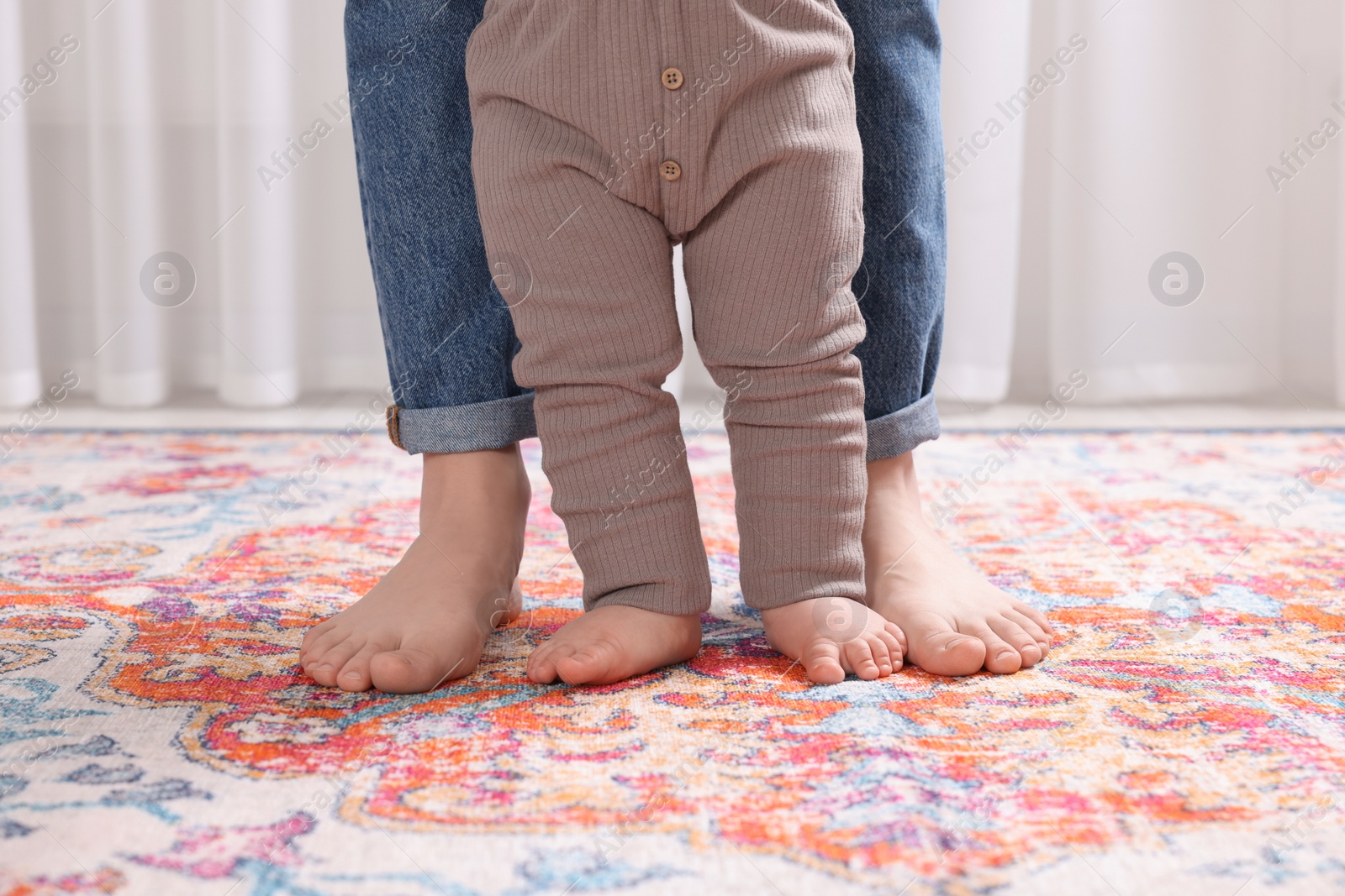 Photo of Mother supporting her baby son while he learning to walk on carpet indoors, closeup