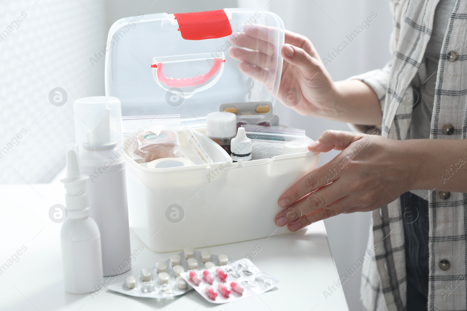 Photo of Woman opening first aid kit at white table indoors, closeup