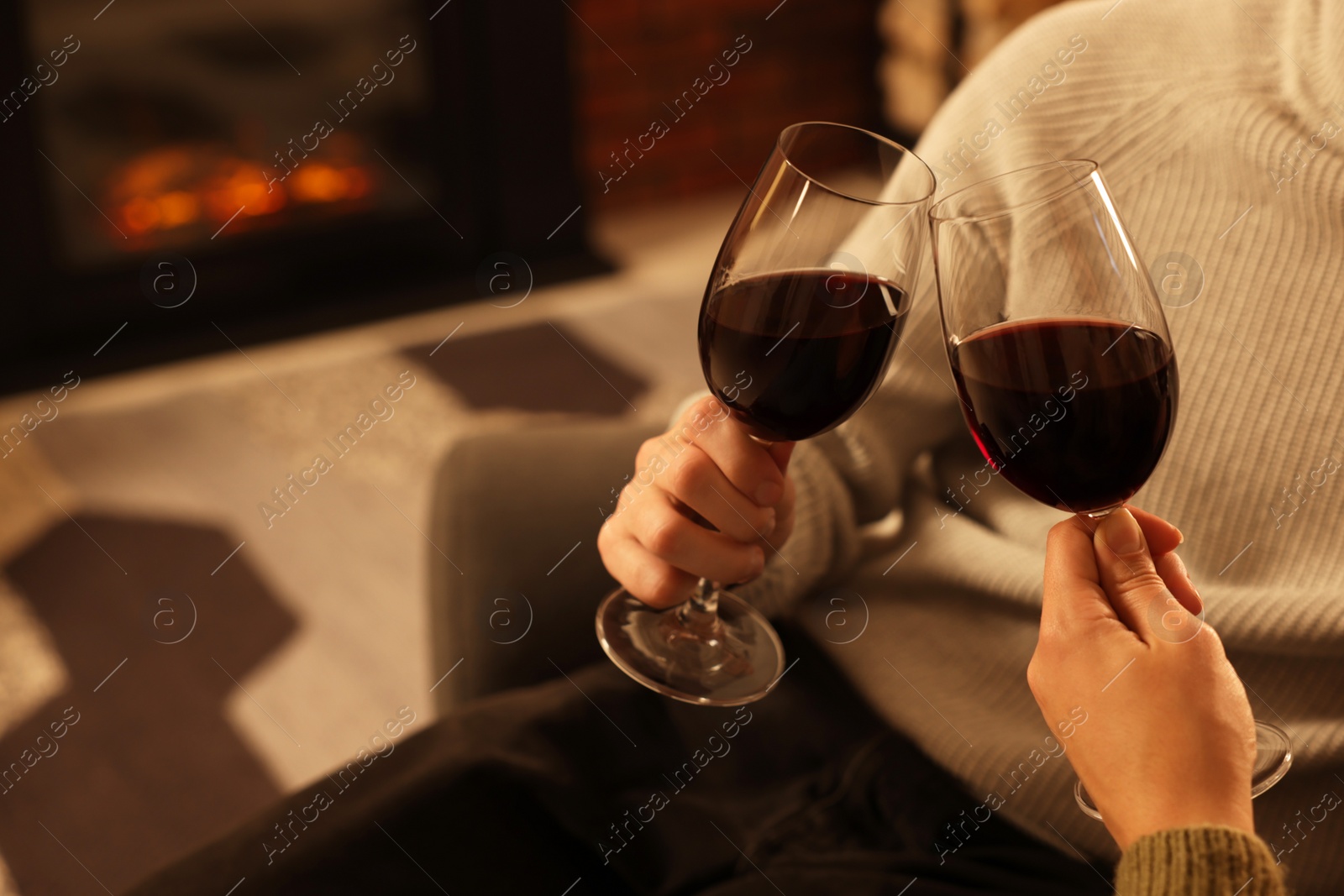Photo of Lovely couple with glasses of wine resting together near fireplace at home, closeup