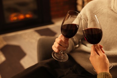 Photo of Lovely couple with glasses of wine resting together near fireplace at home, closeup