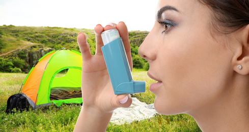 Young woman using asthma inhaler and camping tent in wilderness on background. First emergency medical aid