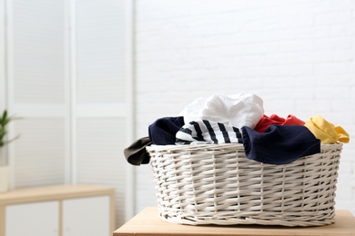 Photo of Laundry basket with dirty clothes on table indoors. Space for text