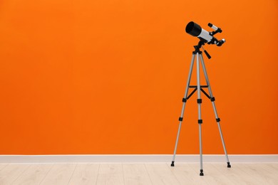 Tripod with modern telescope near orange wall. Space for text