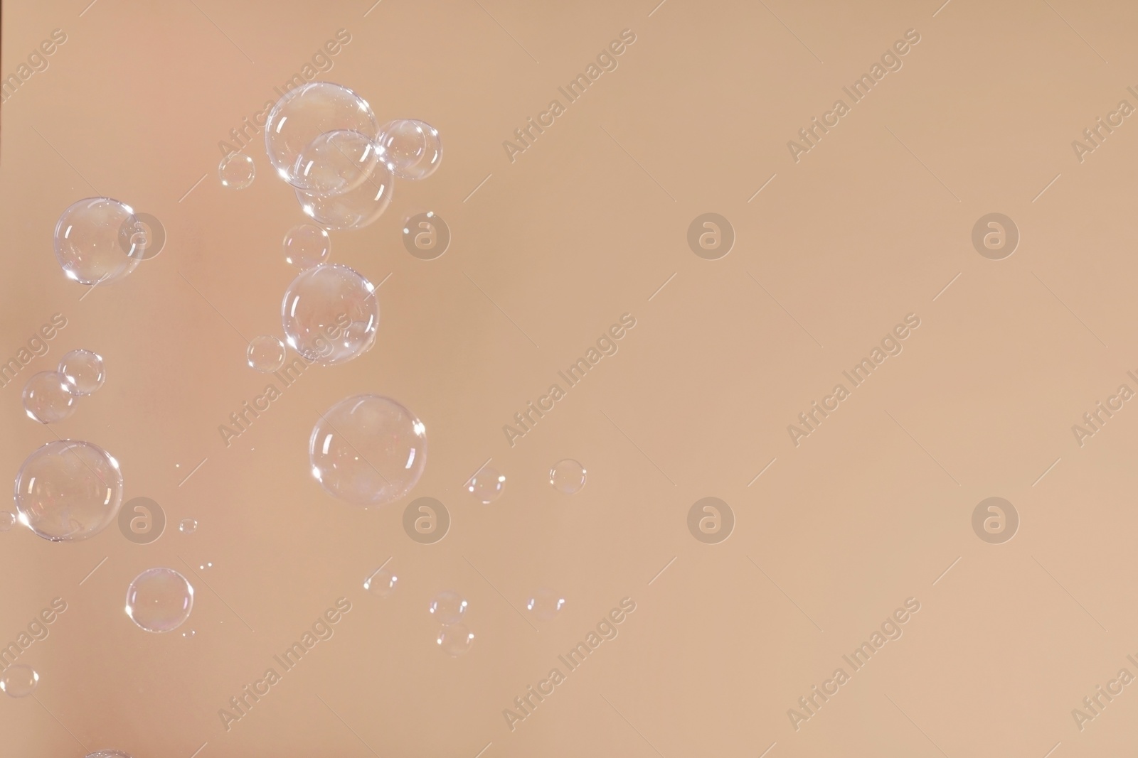 Photo of Many beautiful soap bubbles on light brown background. Space for text