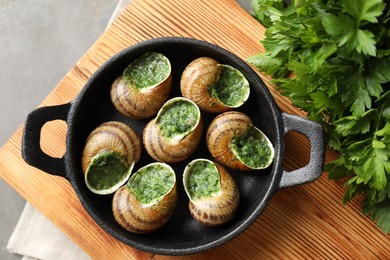 Delicious cooked snails in baking dish and parsley on grey table, flat lay