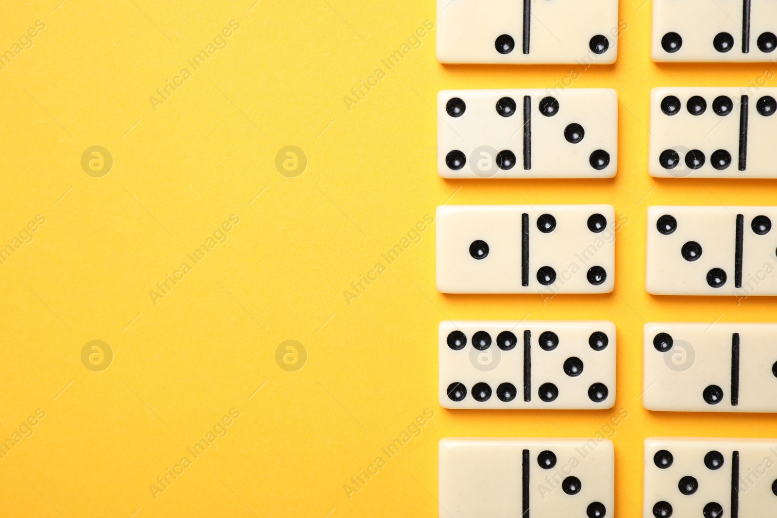 Photo of Classic domino tiles on yellow background, flat lay. Space for text