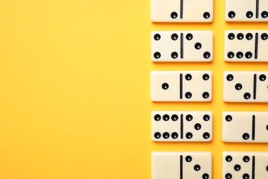 Photo of Classic domino tiles on yellow background, flat lay. Space for text