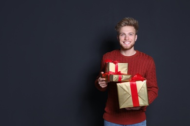 Photo of Young man with Christmas gifts on dark background. Space for text