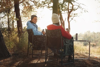 Couple resting in camping chairs and enjoying hot drink outdoors