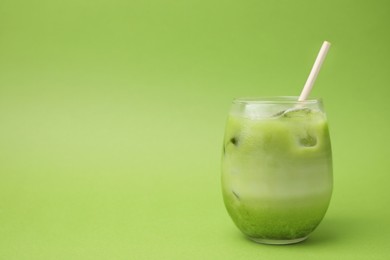 Glass of tasty iced matcha latte on light green background. Space for text