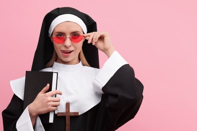 Photo of Woman in nun habit and sunglasses holding Bible against pink background, space for text. Sexy costume