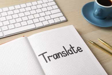 Photo of Word Translate written in notebook, keyboard, cup of coffee and pens on wooden table