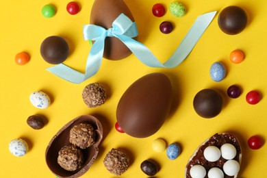 Tasty chocolate eggs and candies on yellow background, flat lay