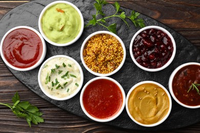 Photo of Different tasty sauces in bowls and parsley on wooden table, top view