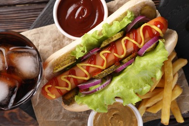 Delicious hot dog with lettuce, onion and pickle served on wooden table, top view