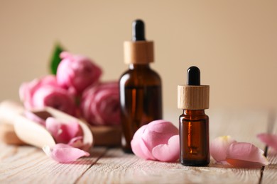 Photo of Bottles of essential oil and roses on white wooden table against beige background