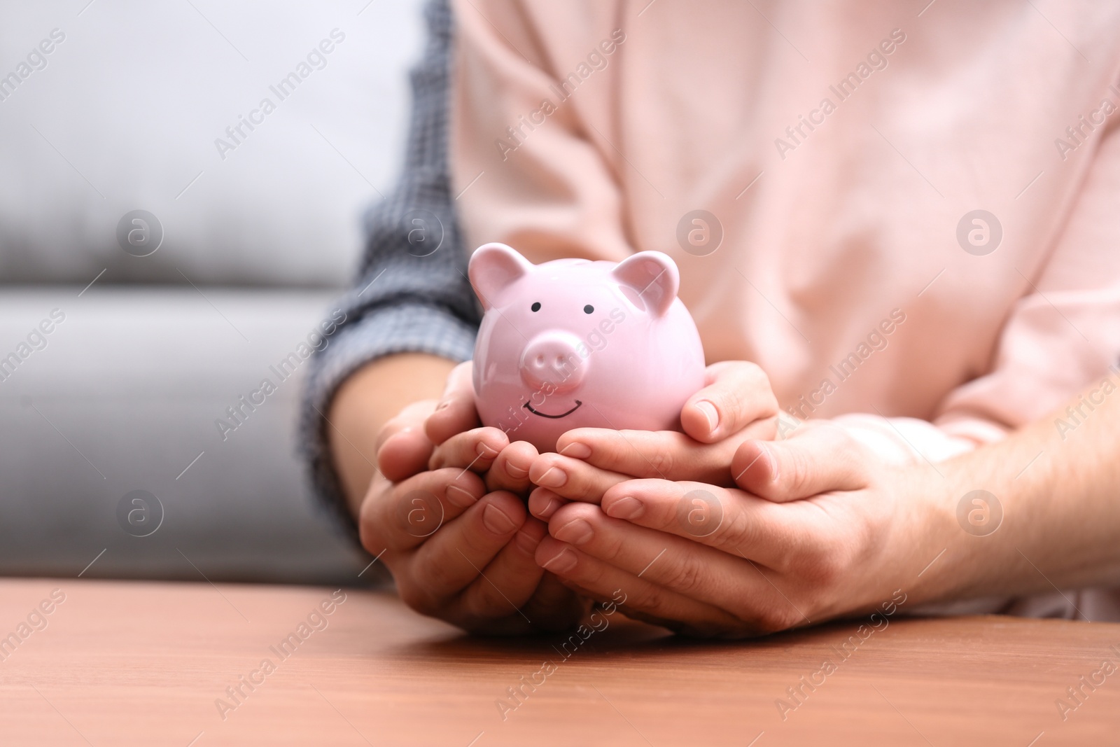 Photo of Couple with piggy bank at wooden table, closeup