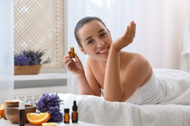 Photo of Happy young woman with bottle of essential oil in spa salon