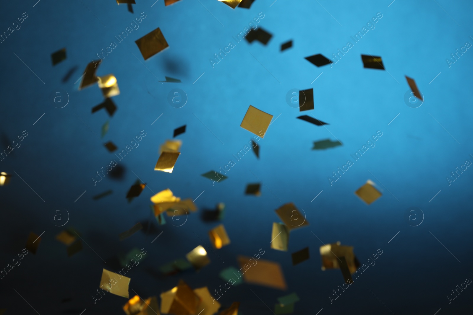 Photo of Shiny golden confetti falling down on blue background