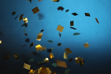 Photo of Shiny golden confetti falling down on blue background