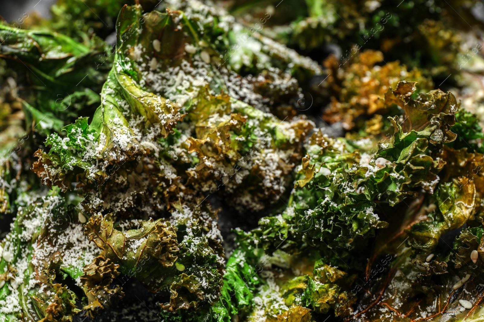 Photo of Tasty baked kale chips with grated cheese as background, closeup