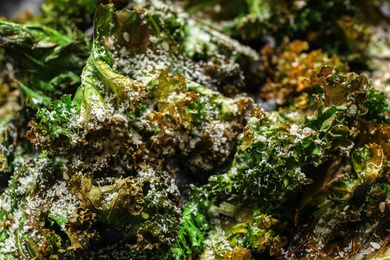 Photo of Tasty baked kale chips with grated cheese as background, closeup