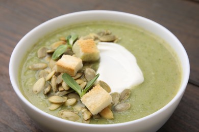 Delicious broccoli cream soup with croutons, sour cream and pumpkin seeds on wooden table, closeup