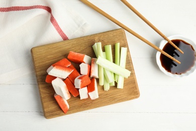 Fresh cut crab sticks with celery served on white wooden table, flat lay