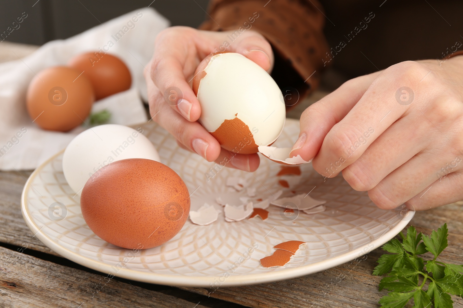 Photo of Woman peeling boiled egg at wooden table, closeup