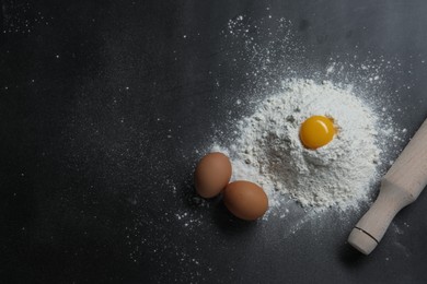 Photo of Flour, rolling pin and eggs on black table, flat lay. Space for text