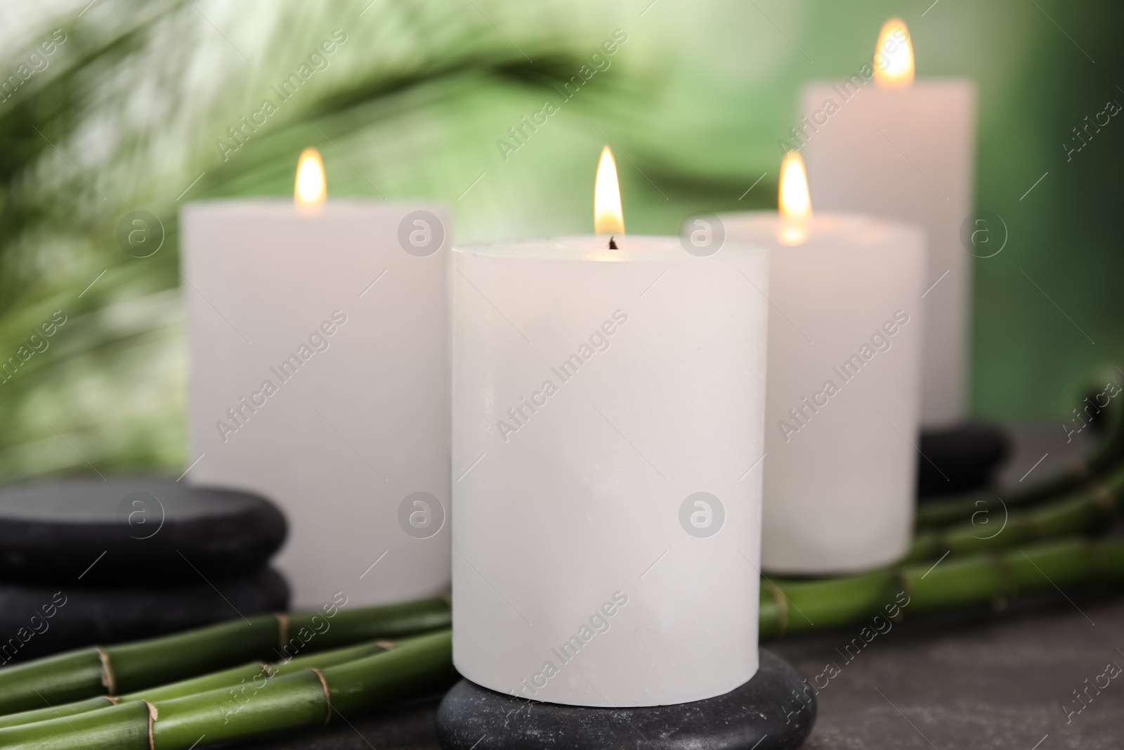 Photo of Burning candles, spa stones and bamboo sprouts on grey table against blurred green background