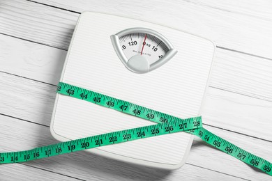 Scales with measuring tape on white wooden background, top view. Weight loss concept