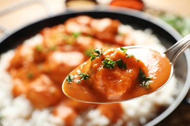 Photo of Tasty butter chicken in spoon over dish with meal, closeup