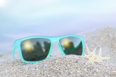 Stylish sunglasses and starfishes on sandy beach, closeup