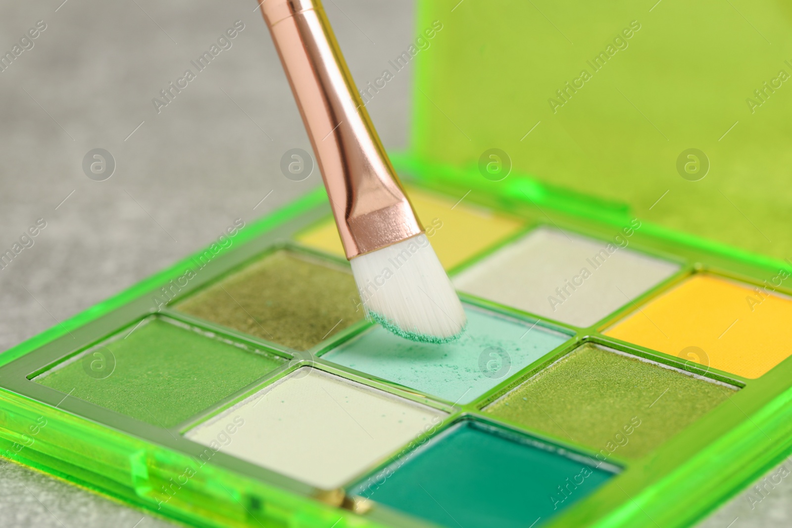 Photo of Colorful eyeshadow palette with brush on grey table, closeup