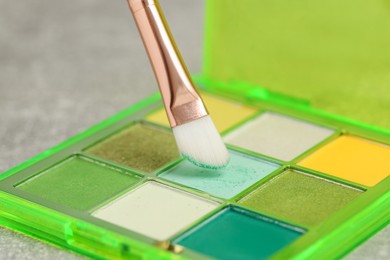 Photo of Colorful eyeshadow palette with brush on grey table, closeup