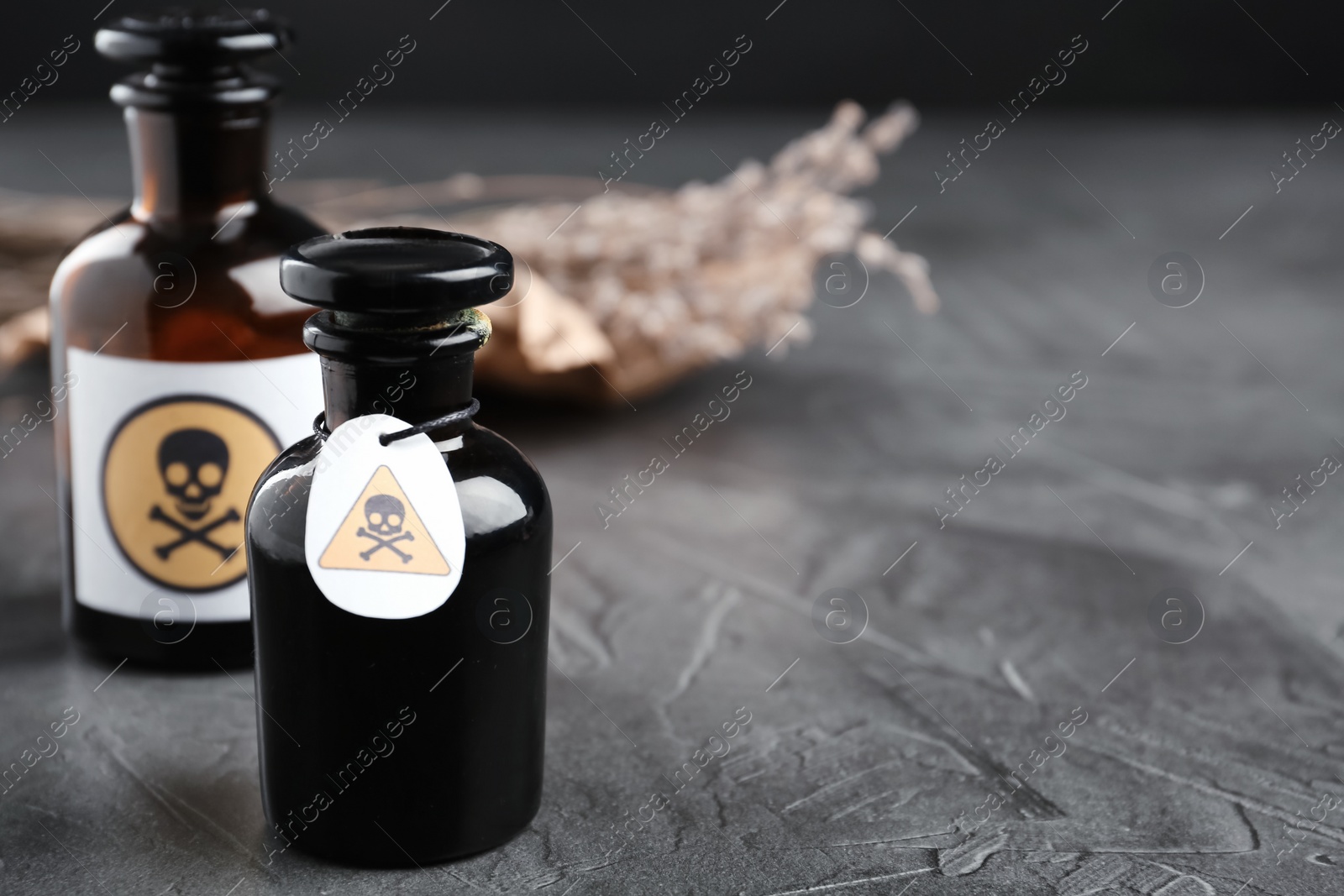 Photo of Glass bottles of poison with warning signs on grey stone table. Space for text