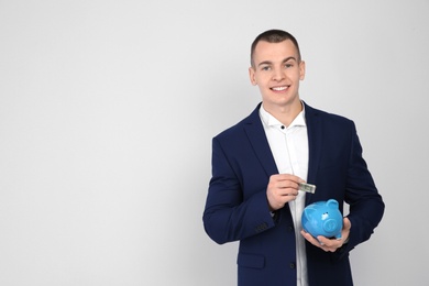 Photo of Young businessman putting money into piggy bank on white background. Space for text
